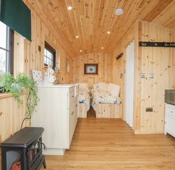 A small wooden room with two single beds a kitchenette with a sink a microwave on a small cabinet and a black heater at Tal Sarn Shepherd Hut in Dwyran near Niwbwrch Newborough