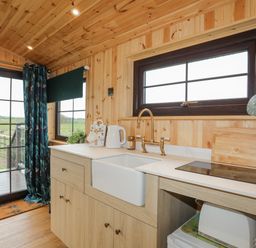 A kitchen area with a farmhouse sink stovetop and cabinets in a wooden room at Tal Sarn Shepherd Hut Dwyran near Niwbwrch Newborough