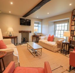 A living room with sofas, armchairs, lamps, a coffee table, bookshelves, and a wall-mounted TV at Green Yew in Winster near Bowness-On-Windermere