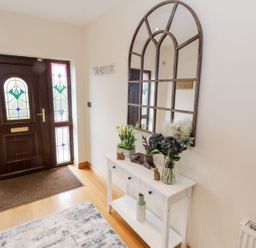 An entryway with a wooden door featuring stained glass panels a white console table with flowers and decorative items and a large arched mirror on the wall at Doonalton House in Dromore West County Sligo