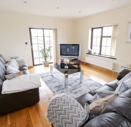 A living room with two black leather sofas a glass coffee table a rug a TV and windows at Doonalton House in Dromore West County Sligo
