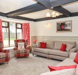 A living room with beige sofas red cushions and plaid armchairs near a window at Nempnett Farmhouse in Nempnett Thrubwell near Blagdon