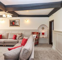 A living room with beige sofas and red cushions and a plaid armchair with a red lamp at Nempnett Farmhouse Nempnett Thrubwell near Blagdon