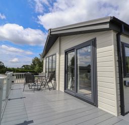 An outdoor deck with a table and four chairs next to a beige building with large windows and sliding glass doors at Lodge 3 in St Asaph