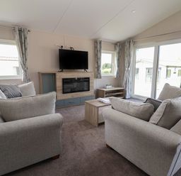 A living room with two sofas a TV on a stand a coffee table and windows with curtains at Lodge 3 in St Asaph