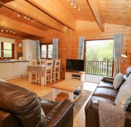 A living area with leather sofas a wooden coffee table dining table and kitchen inside a wooden cabin at Kingfisher Lodge in Badwell Ash