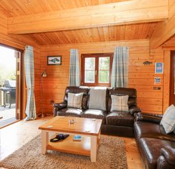 A wooden living room with leather sofas a coffee table and a television at Woodpecker Lodge in Badwell Ash