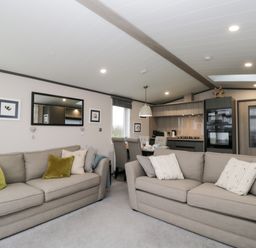 A living room with two beige sofas and a dining area with chairs and kitchen appliances at Tiggywinkles in Chipping Norton