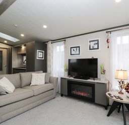 A living room with a beige sofa a tv on a stand with an electric fireplace and a side table with a lamp and flowers at Tiggywinkles in Chipping Norton