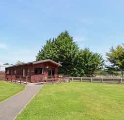 An outdoor view of a log cabin with grass and trees at The Fallows near Llanerch Park near St Asaph