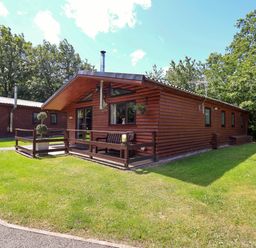A log cabin with outdoor seating and trees in the vicinity at The Roe in Llanerch Park near St Asaph