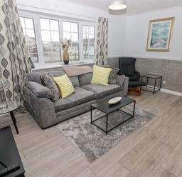 A living room with a gray sofa and yellow cushions a black chair a coffee table and a television at 48 Gower Holiday Village in Scurlage