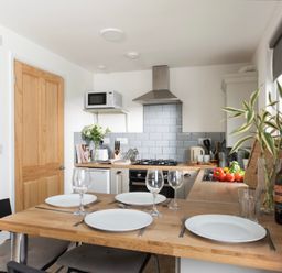 A kitchen with a wooden dining table set for four near a stove and a microwave at Bushwood Lodge in Wendron near Helston