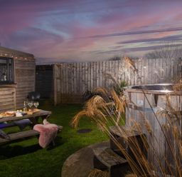 An outdoor area with a wooden picnic table set with food and drinks a wooden hot tub and a fence at Wheal Jewel Lodge in Wendron near Helston