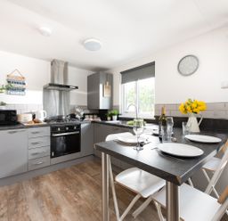 A kitchen with grey cabinets and a black countertop with a dining table set for four at Wheal Prosper Lodge in Wendron near Helston