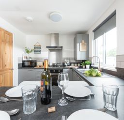 A kitchen with a dining table set with plates glasses and a bottle of wine at Wheal Rose Lodge in Wendron near Helston