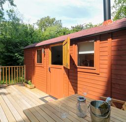 A wooden deck with a table and chairs outside a wooden hut at The Foxes Den Shepherds Hut in Oldbury-On-Severn