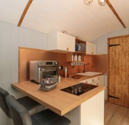 A kitchen with wooden countertops and cabinets two black chairs a metal toaster oven and a wooden door at The Foxes Den Shepherds Hut in Oldbury-On-Severn