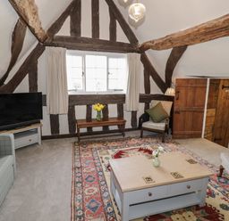 A living room with wooden beams a television sofas a coffee table and a patterned rug at The Bindery in Broadway