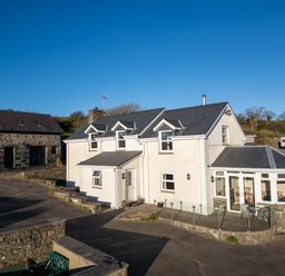 A white two-story house with dormer windows and a glass conservatory next to a stone building at Crogal Farmhouse in New Quay