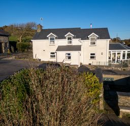 A white two-story house with dormer windows and a stone building nearby at Crogal Farmhouse in New Quay
