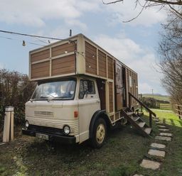 A converted vintage truck with wooden paneling and stairs leading to a door parked on grass with trees and string lights at Sea the Stars in New Quay