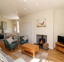 A living room and kitchen area with armchairs a coffee table a wood stove and a dining table at 2 Twizel Station Cottage in Cornhill-on-Tweed near Norham