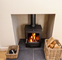 A wood burning stove with fire inside and two wicker baskets one with firewood the other with tools at 2 Twizel Station Cottage in Cornhill-on-Tweed near Norham