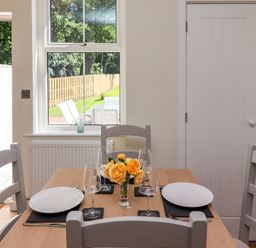 A dining table set with plates wine glasses and a vase of yellow roses in a room with a window and white doors at 2 Twizel Station Cottage in Cornhill-on-Tweed near Norham