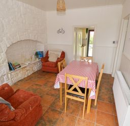 A dining room with a table covered with a red and white checkered tablecloth and four chairs two armchairs and a white stone fireplace at Marys Cottage Theur near Riverstown County Sligo