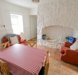 A dining room with a red checkered tablecloth on the table two orange armchairs and a white stone fireplace at Marys Cottage Theur near Riverstown County Sligo