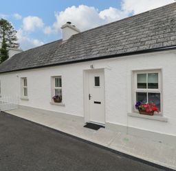 Exterior front view of a white single-story cottage with three windows flower boxes and a door at Marys Cottage Theur near Riverstown County Sligo
