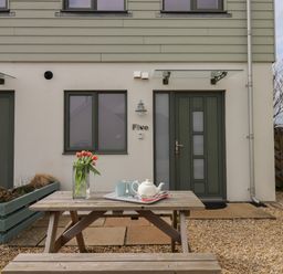 A wooden picnic table with a vase of tulips and tea set outside a house with green doors and windows at 5 Ocean Reach in Bolberry