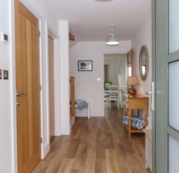 A hallway with wooden doors wooden floor a side table with a lamp a round mirror and a bench at 5 Ocean Reach in Bolberry