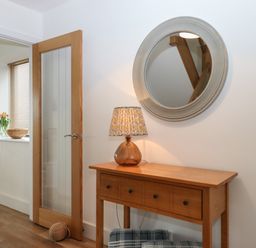 An entryway with a wooden console table a lamp a round mirror and a wooden door at 5 Ocean Reach in Bolberry