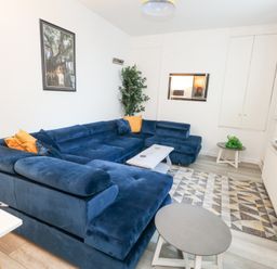 A living room with a blue sectional sofa yellow pillows two round tables and a wall-mounted tv at Beachaven in Weymouth
