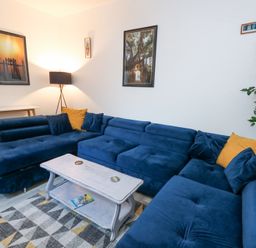 A living room with a blue sectional sofa and yellow pillows a white coffee table and a floor lamp at Beachaven in Weymouth
