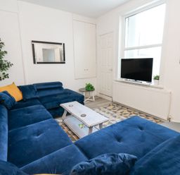 A living room with blue sectional sofa a coffee table a flat screen TV and a large window at Beachaven in Weymouth