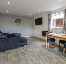 A living room with a dark sofa a wooden dining table with chairs and a wall mounted tv at Classic Lodge 25 in Dyserth