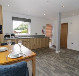 A kitchen with wooden cabinets a dining table set for two and a door open to outside at Classic Lodge 25 in Dyserth