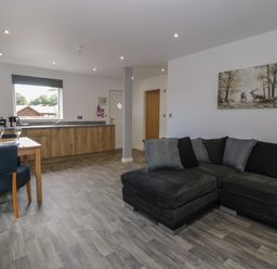 An open plan kitchen and living area with a black sofa and wooden dining table at Classic Lodge 25 in Dyserth