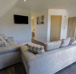 A living room with two gray sofas facing a wall mounted television and a wooden door at Premier Lodge 41 in Dyserth