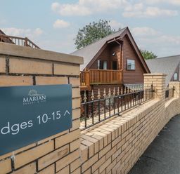 A brick wall with a sign indicating lodges 10-15 and wooden lodges behind the wall at Classic Lodge 15 in Dyserth