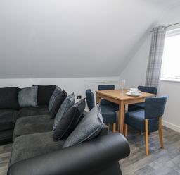A living room with a black sofa and a wooden dining table with blue chairs near a window at Classic Lodge 15 in Dyserth