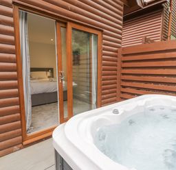 An outdoor hot tub next to a wooden cabin with sliding glass door leading to a bedroom at Luxury Lodge 46 in Dyserth