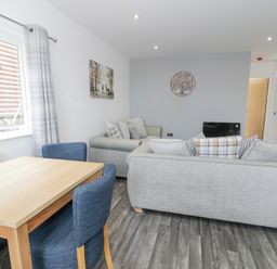 A living room with grey sofas blue dining chairs and a wooden table at Luxury Lodge 46 in Dyserth