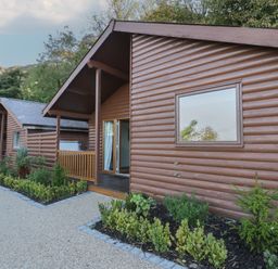 A row of wooden log cabins with small porches and garden beds along a gravel path at Luxury Lodge 53 in Dyserth