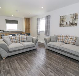 A living room with two sofas and a kitchen area with wooden cabinets at Luxury Lodge 62 in Dyserth