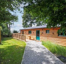 A cabin with a pathway leading to a door surrounded by grass and trees at Owl Lodge Menheniot