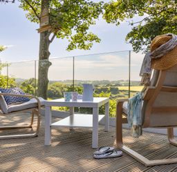 A deck with two chairs and a table overlooking a scenic view at Owl Lodge Menheniot